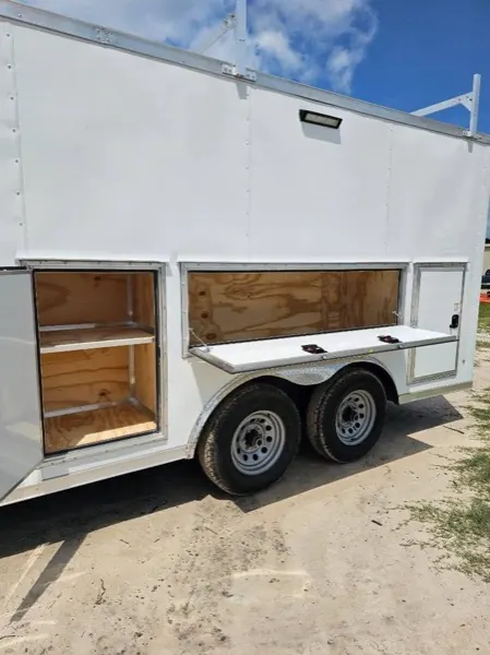 White contractor trailer with its side hatches propped open, showing the plywood lined compartments