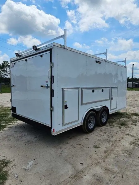White tandem axle contractor trailer with a roof ladder rack and side access doors, rear three-quarter view
